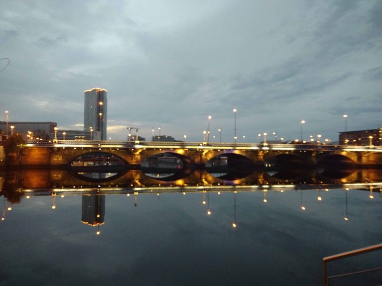 Un pont éclairé et les lumières de la ville se reflètent dans l'eau.