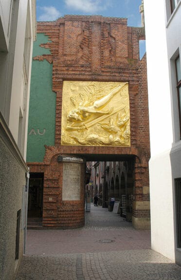 Bronze textured sculpture of a war angel with a sword on a reddish brown brick wall at the entrance of the Böttcherstraße in Bremen 