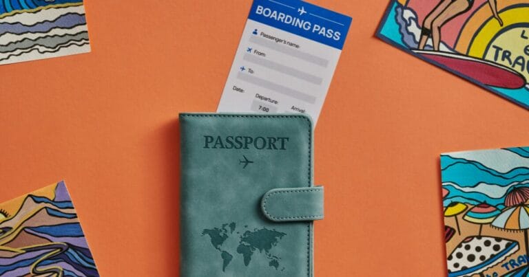 Empty boarding pass and a passport with postcards around on an orange background.