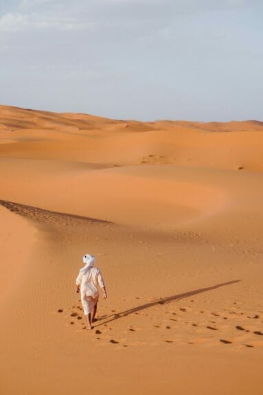 A man walking across sand dunes in Merzouga, Morocco.