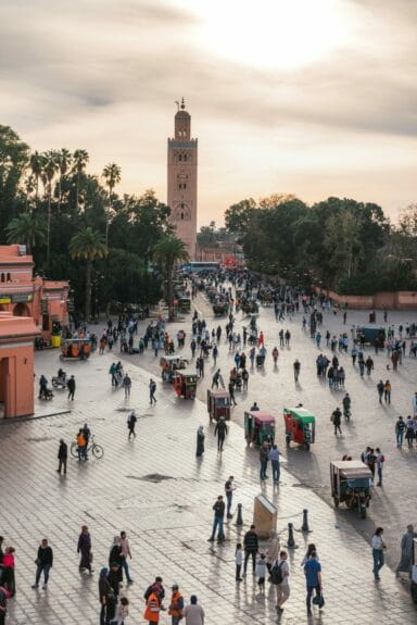 A large group of people walking around Jemaa el-Fna in Morocco with a mosque in the background.