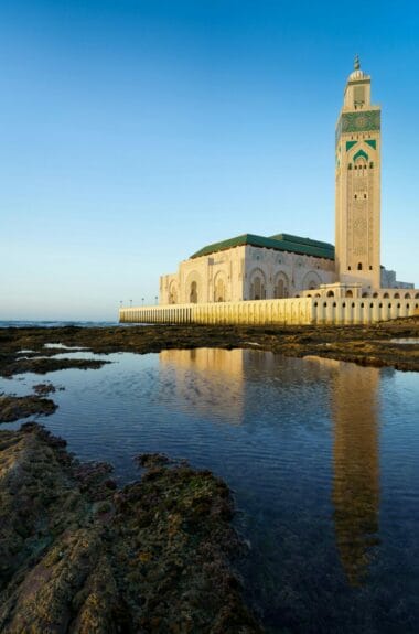 Hassan II Mosque with its reflection on the water in Casablanca, Morocco under the blue sky.