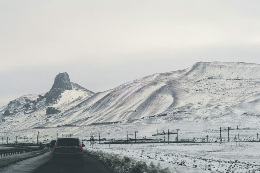 A gray car on the road with mountains covered in snow ahead in Quba, Azerbaijan.