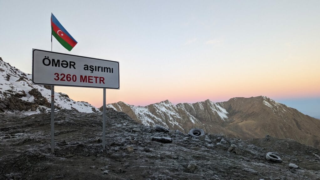 A mountain range covered in snow with a sign and Azerbaijan flag on top.