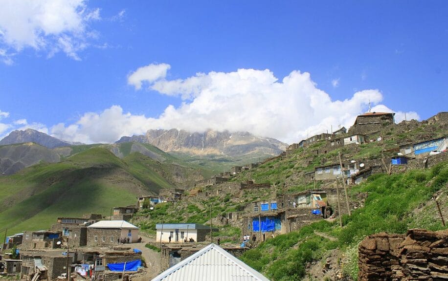 Houses on a hill with mountains in the background under the blue sky in Khinalug, Azerbaijan.