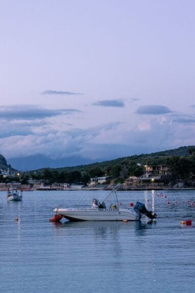 Two boats floating on a body of water in Ksamil Beach, Albania with houses and mountains in the background.