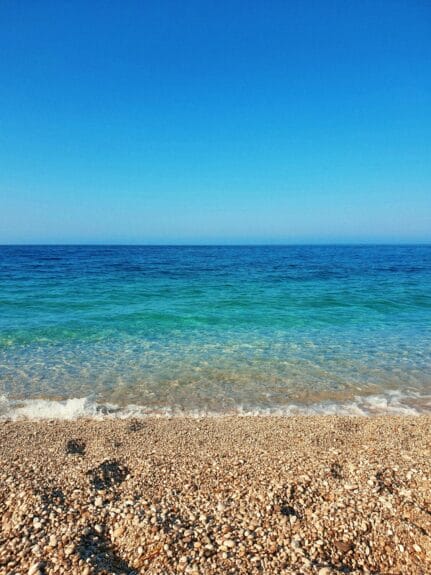 Turquoise waters of the Drymades Beach, Albania under the blue sky crashing on the brown rocky sands.