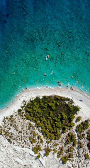 Aerial view of Palasa Beach, Albania with clear blue waters and moss-covered rocks on the shore.