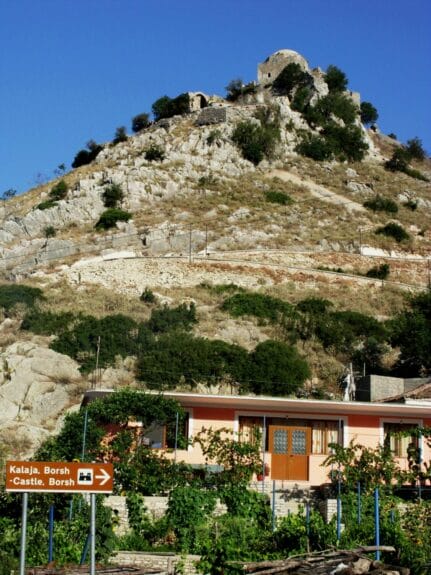 Ruins of the Borsh Castle at the top of the hill with a house at the foot of the mountain in Albania.