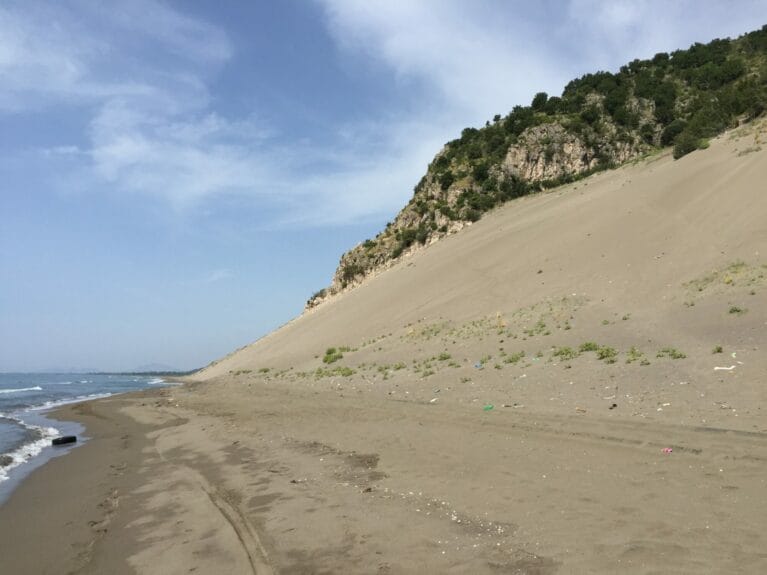 Rana e Hedhun dunes in Albania that rise towards the mountains with scattered trees.