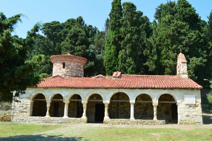 Zvernec Monastery (a church made from stones) with huge trees in the background in Albania.