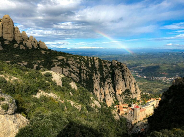 The abbey of Montserrat perched in the mountains with a rainbow crossing the sky