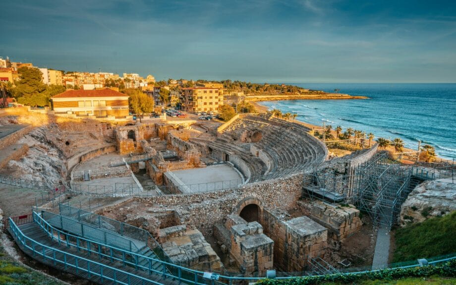 The ruins of a Roman amphitheater in Tarragona under a golden light by the ocean. 