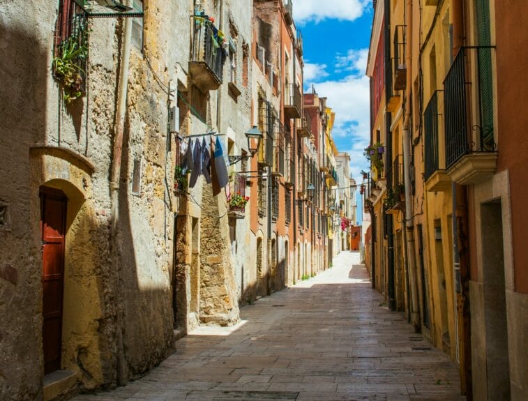 A narrow street in Tarragona with tall old colorful buildings alongside.