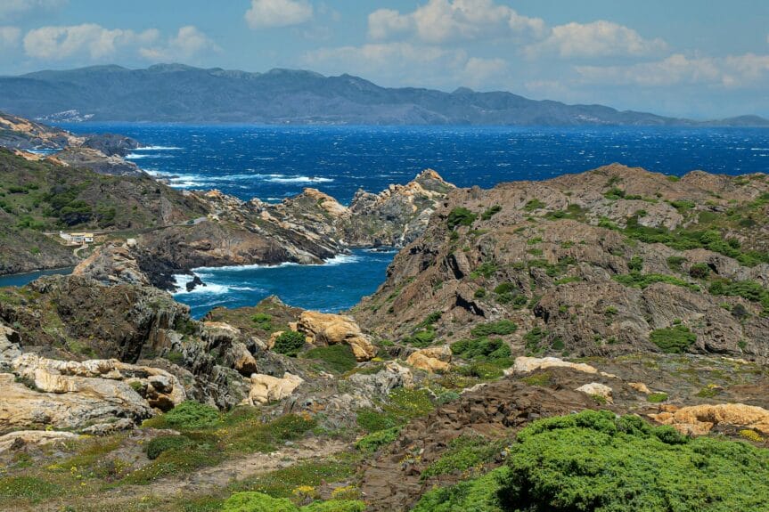 Rocky and hilly island mountain formations in Cap de Creus covered in green with the blue sea between them on a sunny day.