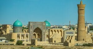 Brown building with blue dome on top and a tower in Bukhara, Uzbekistan.