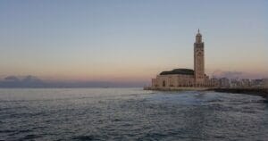 The massive light yellow and green Hassan II Mosque, half on the water, at sunset, in Casablanca, Morocco.