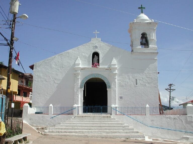 An old white church with colorful houses in the background in Isla Taboga, Panama.