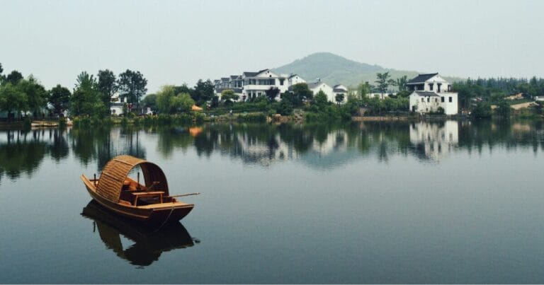 Brown wooden boat on a calm stretch of water overlooking waterfront houses during the day in Nanjing, China.