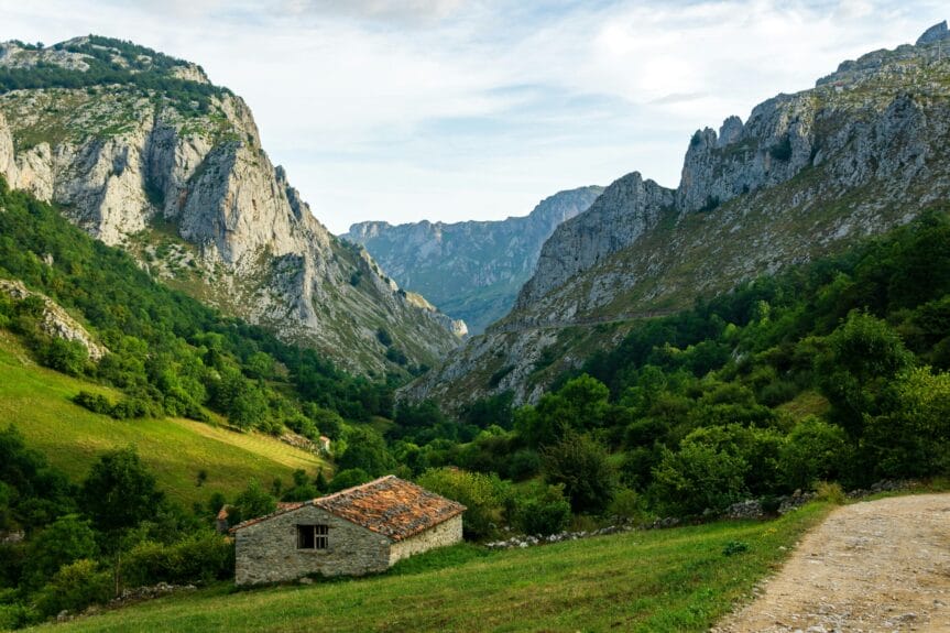 Une maison de briques brunes sur un champ d'herbe verte près d'une montagne sous des nuages blancs dans les Picos de Europa, Espagne.