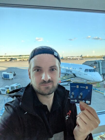 Traveler holding Porter Mastercard cards in front of a Porter Airlines plane parked at the gate.