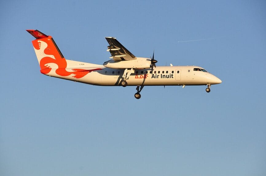Avion DHC-8 d’Air Inuit en vol avec train d’atterrissage sorti, sur fond de ciel bleu.