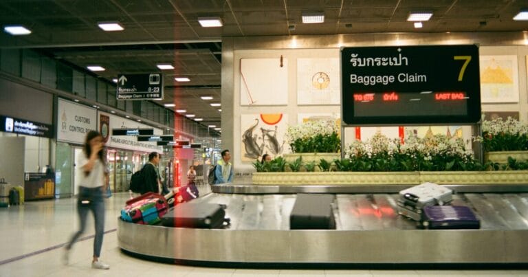 Woman walking in a modern airport terminal at sunrise, pulling a matching set of rolling suitcases toward check-in counters