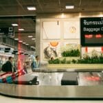 Femme marchant dans un terminal d’aéroport moderne au lever du soleil, tirant un ensemble de valises à roulettes assorties vers les comptoirs d’enregistrement